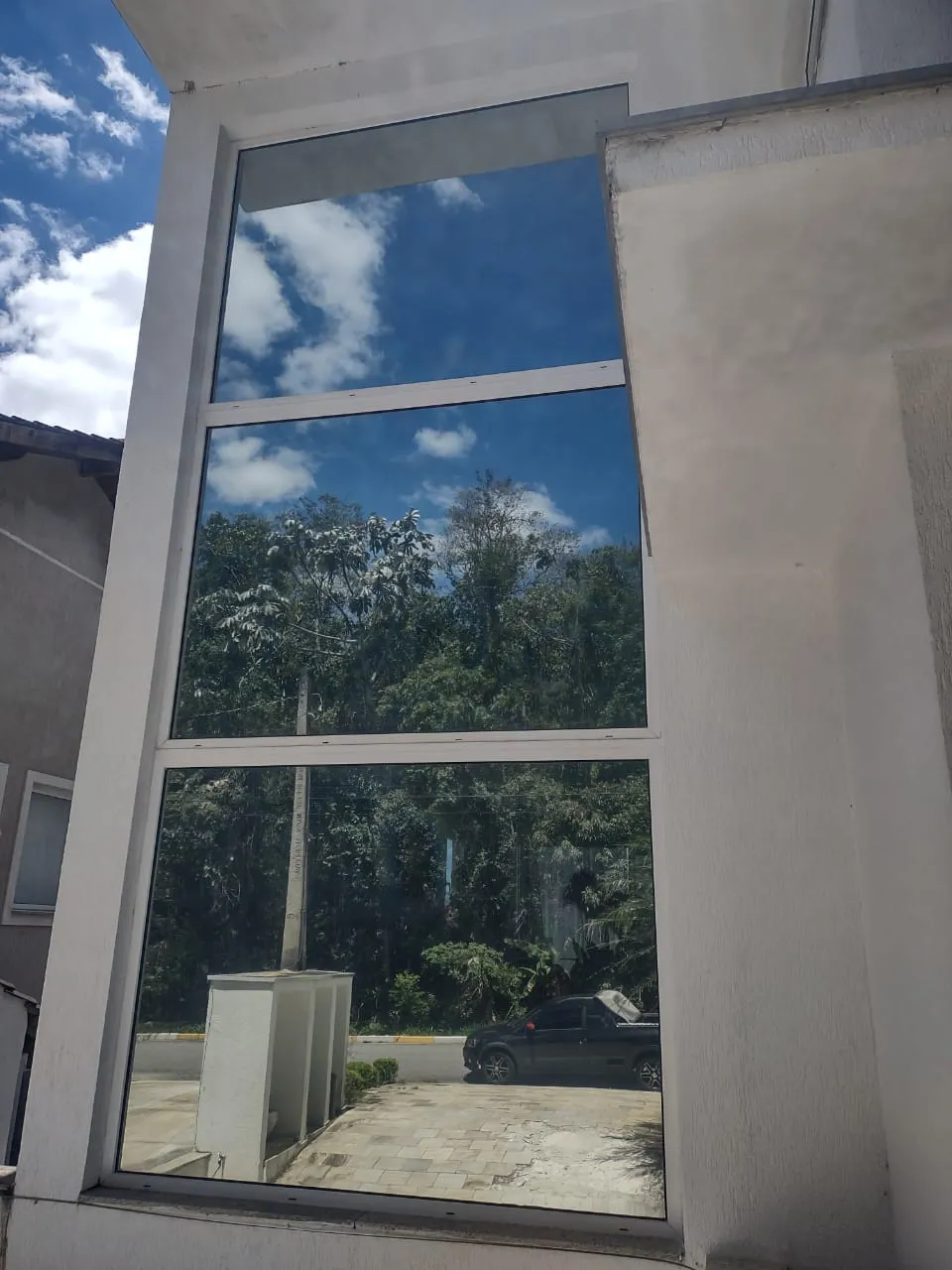 Fachada de vidro com película espelhada refletindo o céu e a vegetação